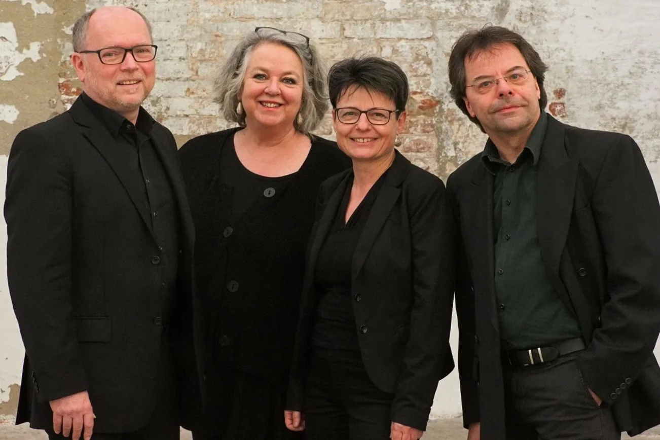 Vier Personen in schwarz gekleidet stehen vor einer Mauer