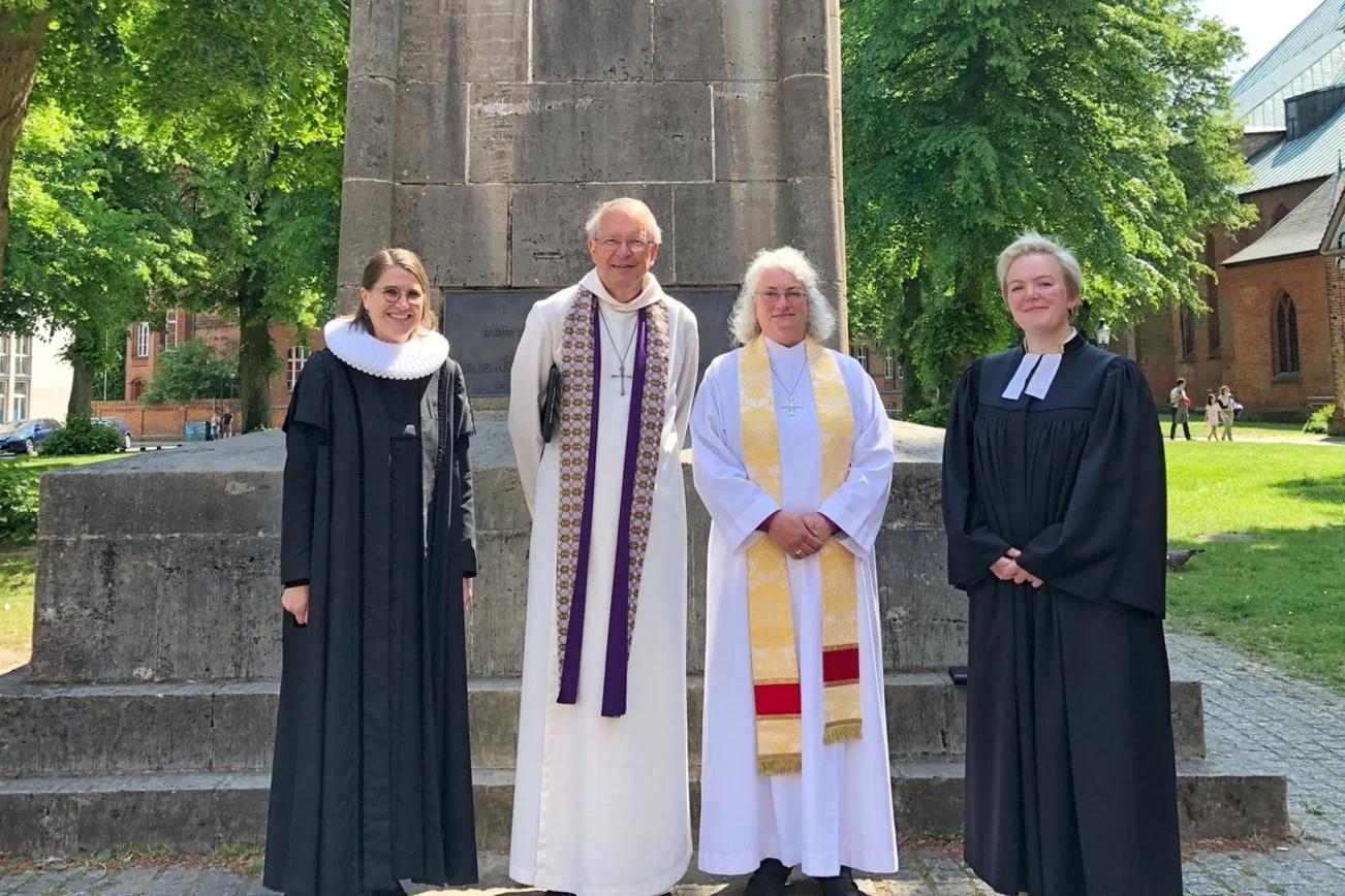 Vier Personen stehen vor einem Denkmal. 