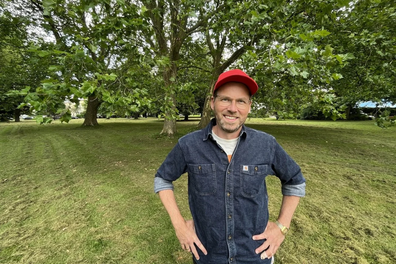 Junger Mann mit Basecap steht in einem grünen Park.