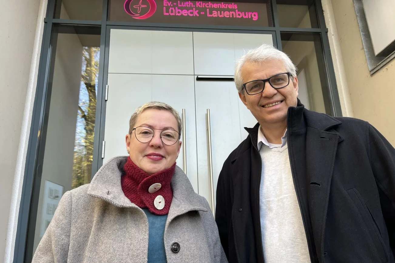 Eine Frau und ein Mann stehen vor einem Gebäude und blicken in die Kamera.