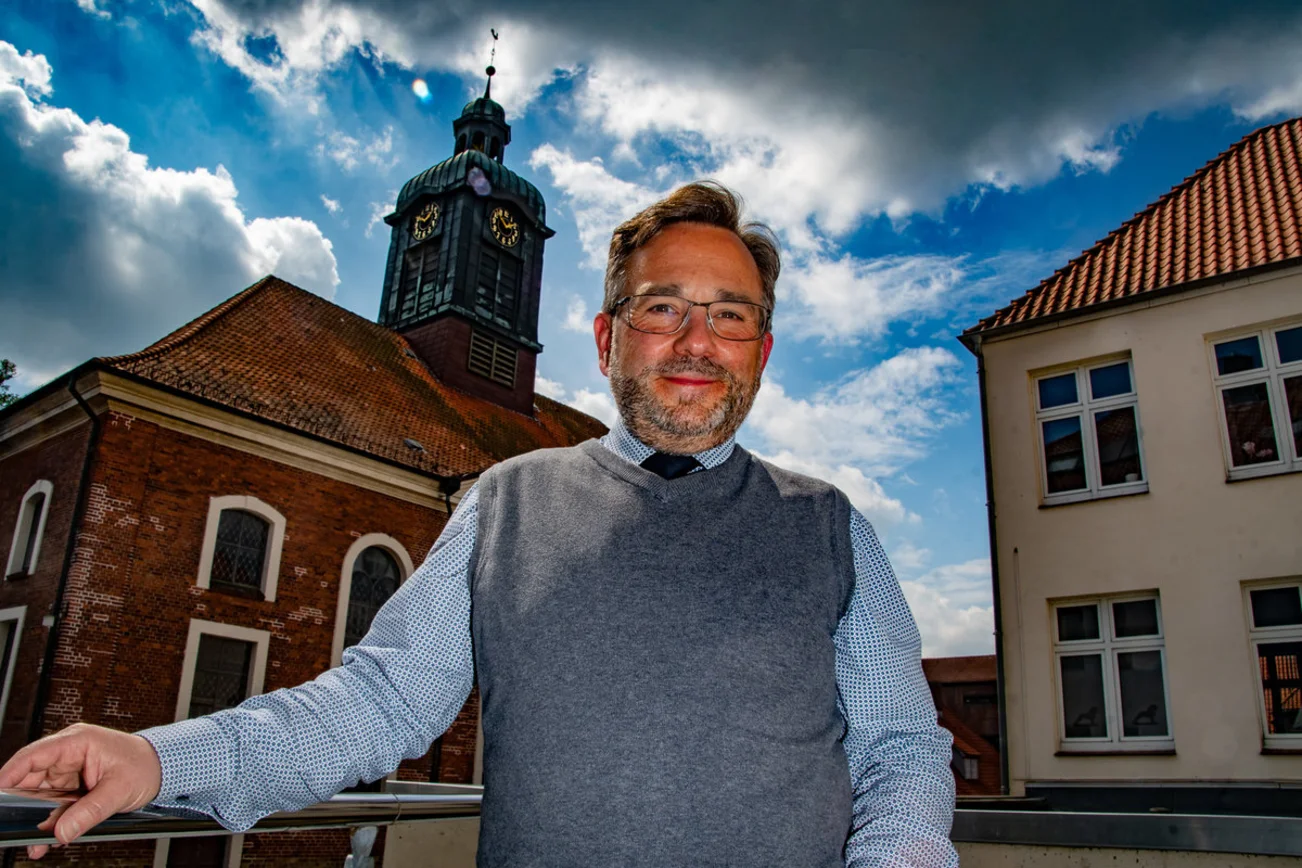 Ein Mann steht lächelnd vor einer Kirche. 