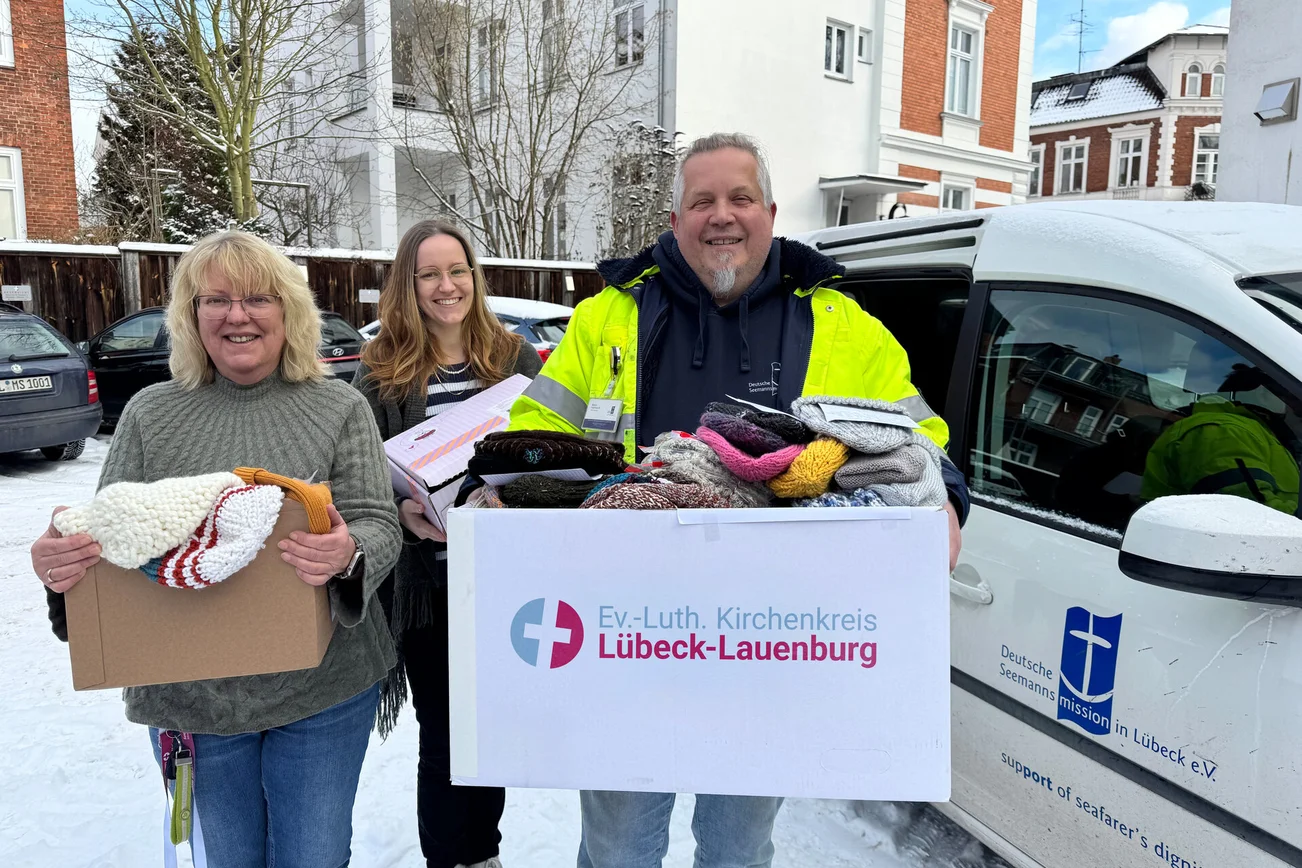 Drei Personen stehen mit Kartons vor einem Auto 