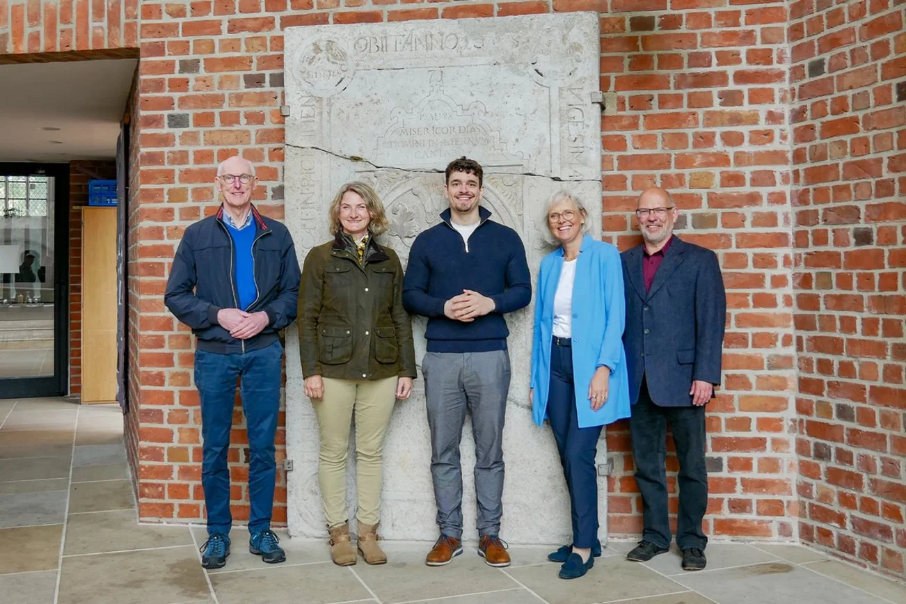 Fünf Personen stehen die Kamera betrachtend vor einer Backsteinmauer
