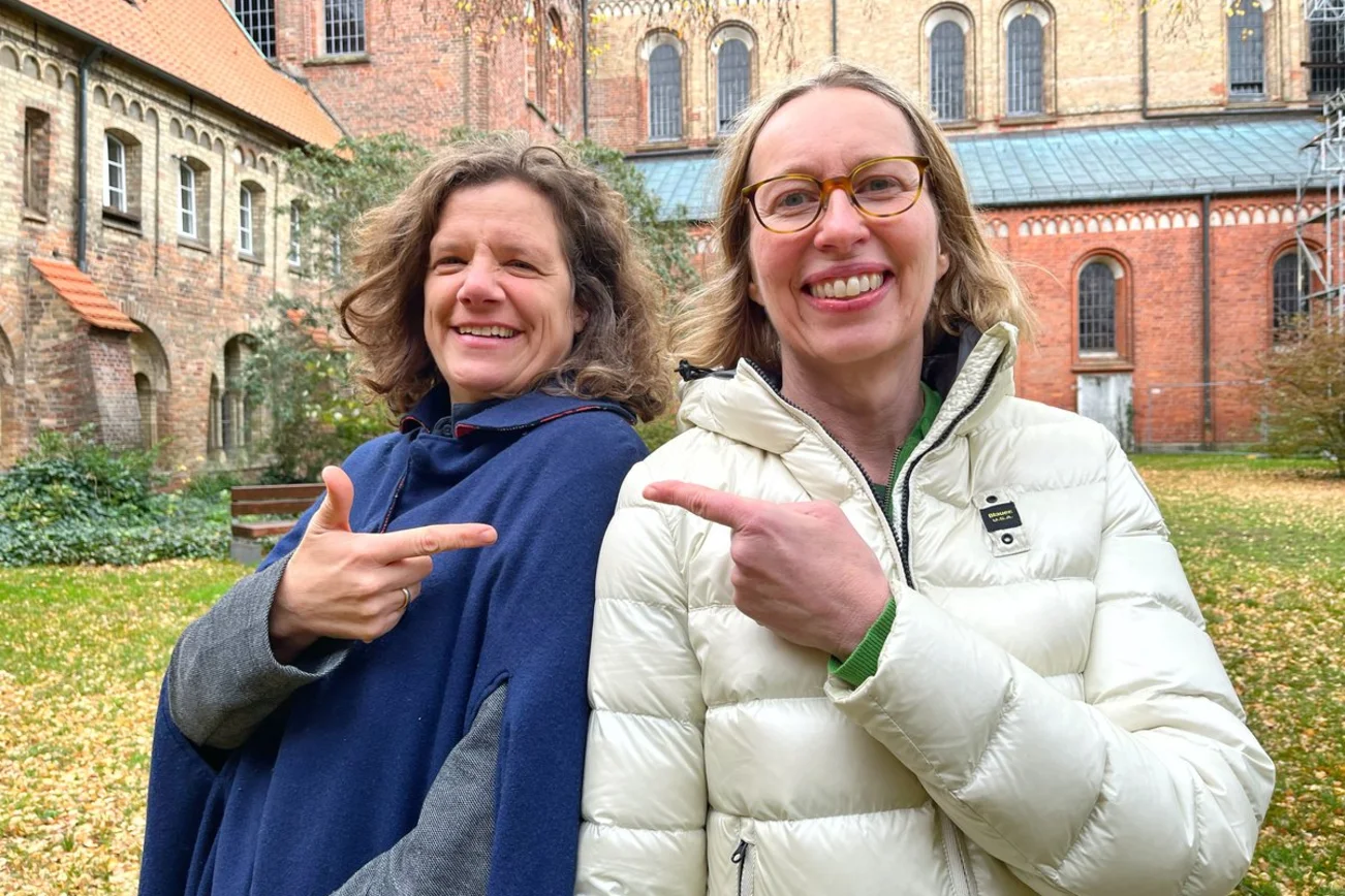 Zwei Personen stehen in einem Kirchenchor und lächeln in die Kamera.