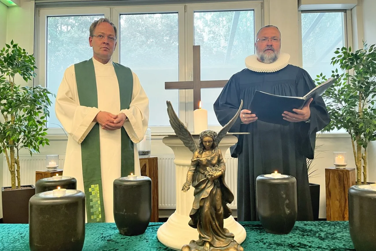 Zwei Pastoren in einem Raum vor einem Tisch mit Urnen