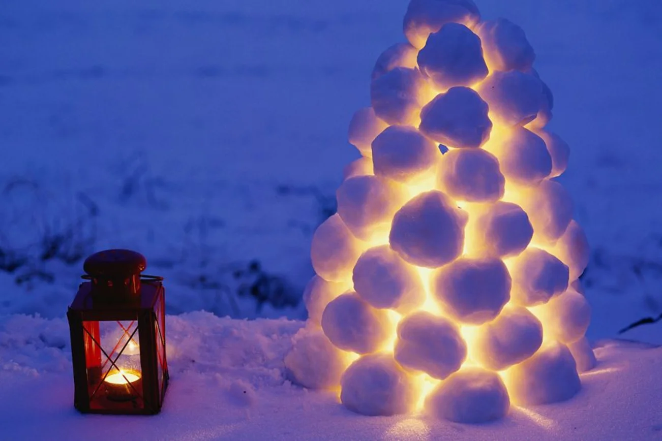 Eine rote Metalllaterne steht im Schnee neben einer Schneeball-Laterne