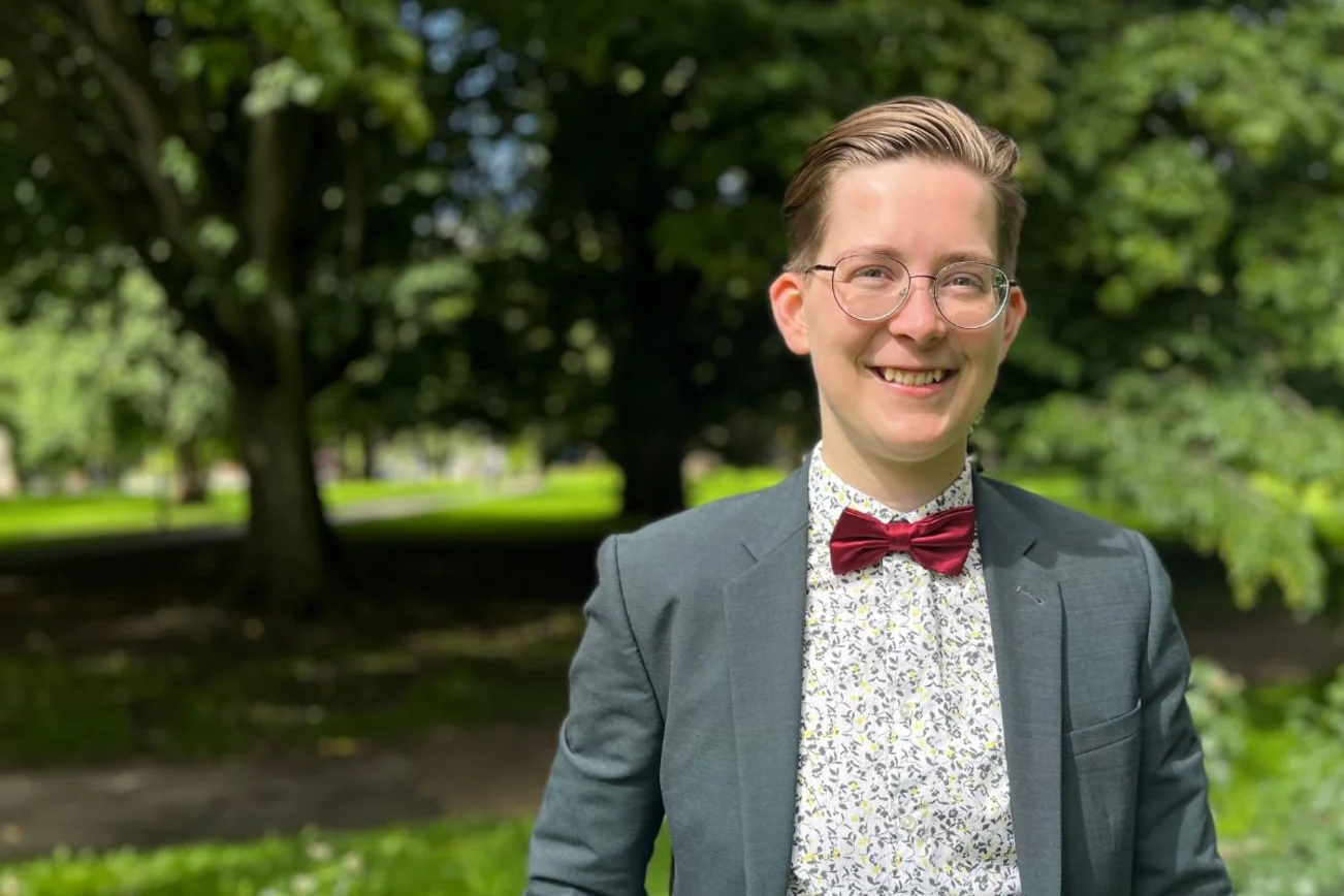 Ein junger Mann mit kurzen Haaren, blauem Sakko und roter Fliege. 