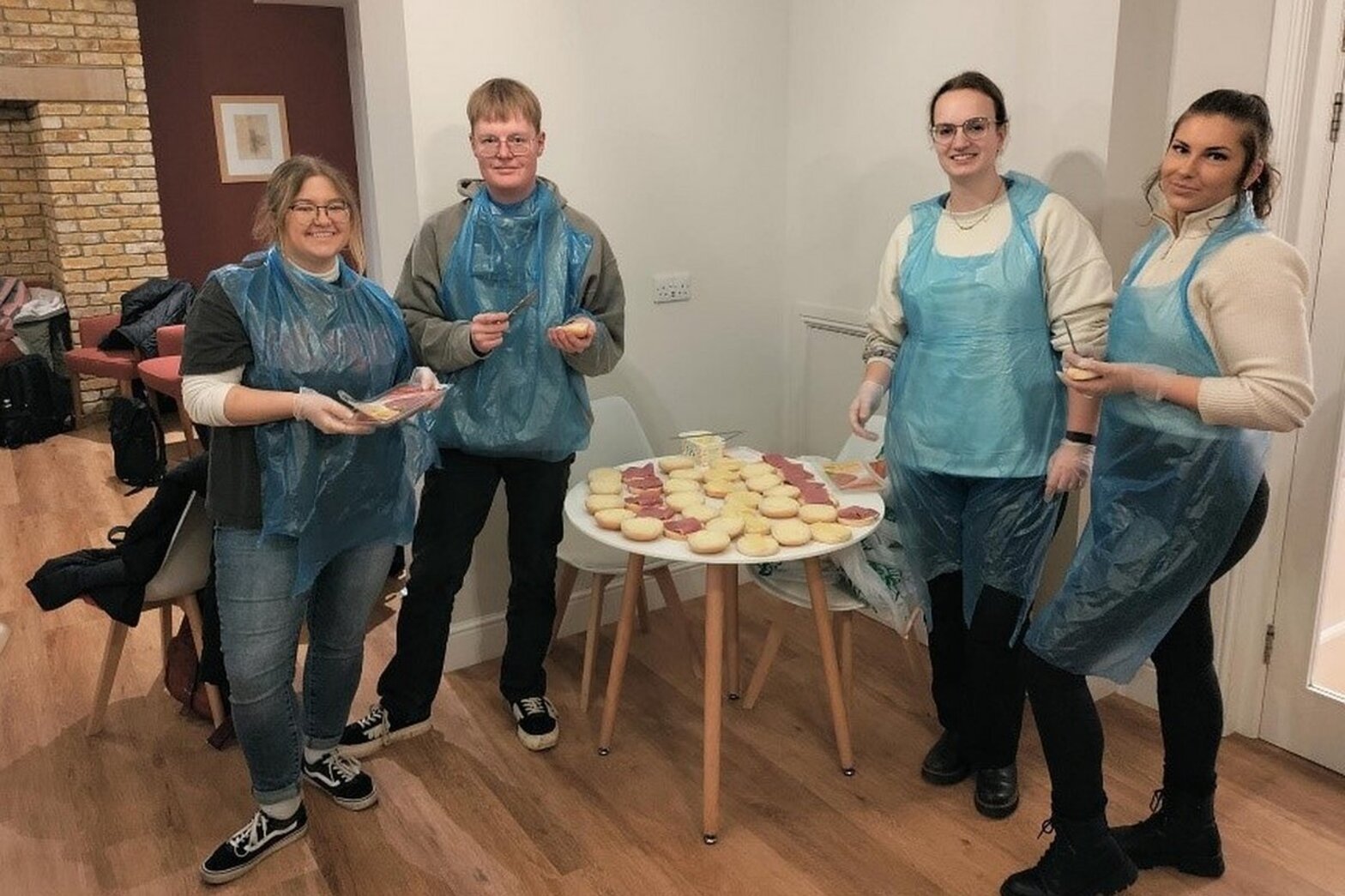 Vier junge Menschen mit blauen Plastikschürzen schmieren Brötchen.