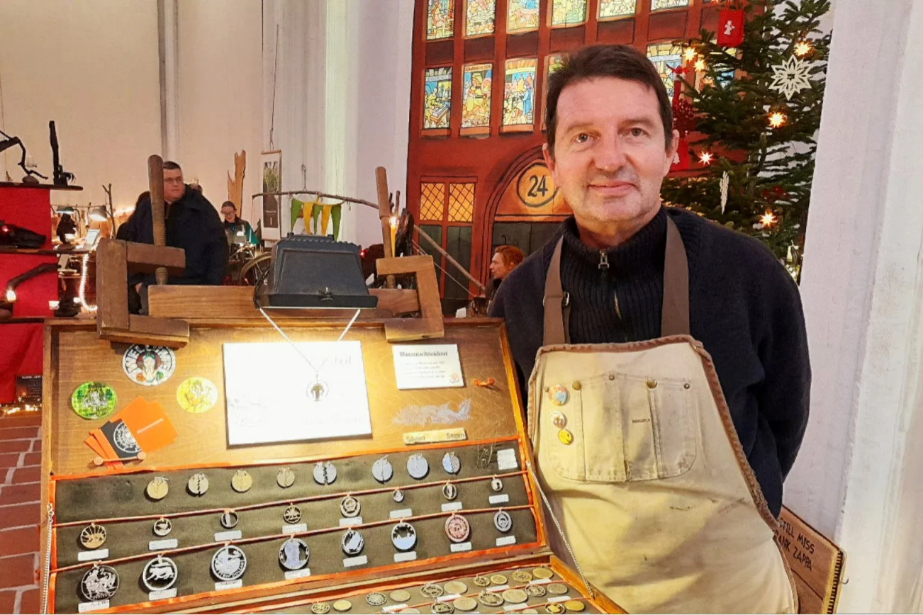 Ein Mann mit Schürze steht nehmen einem Koffer voller Münzanhänger