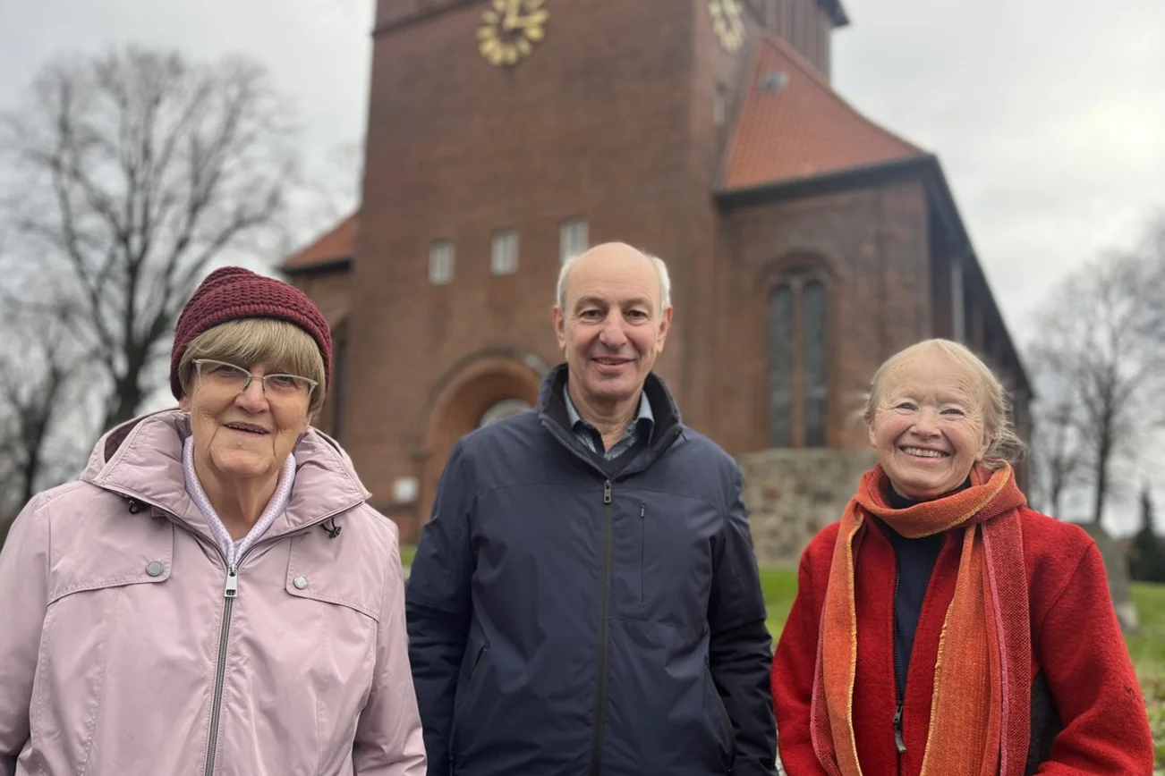 Zwei Frauen und ein Mann stehen im Winter vor einer Kirche.