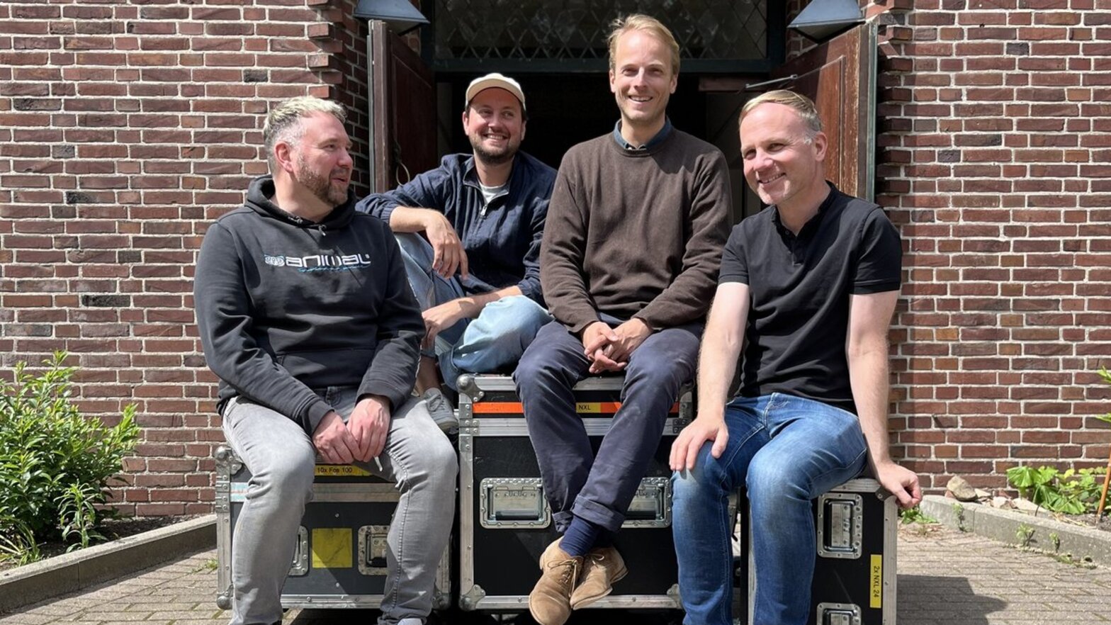 Vier Männer sitzen vor einer Kirche auf Technik-Containern.