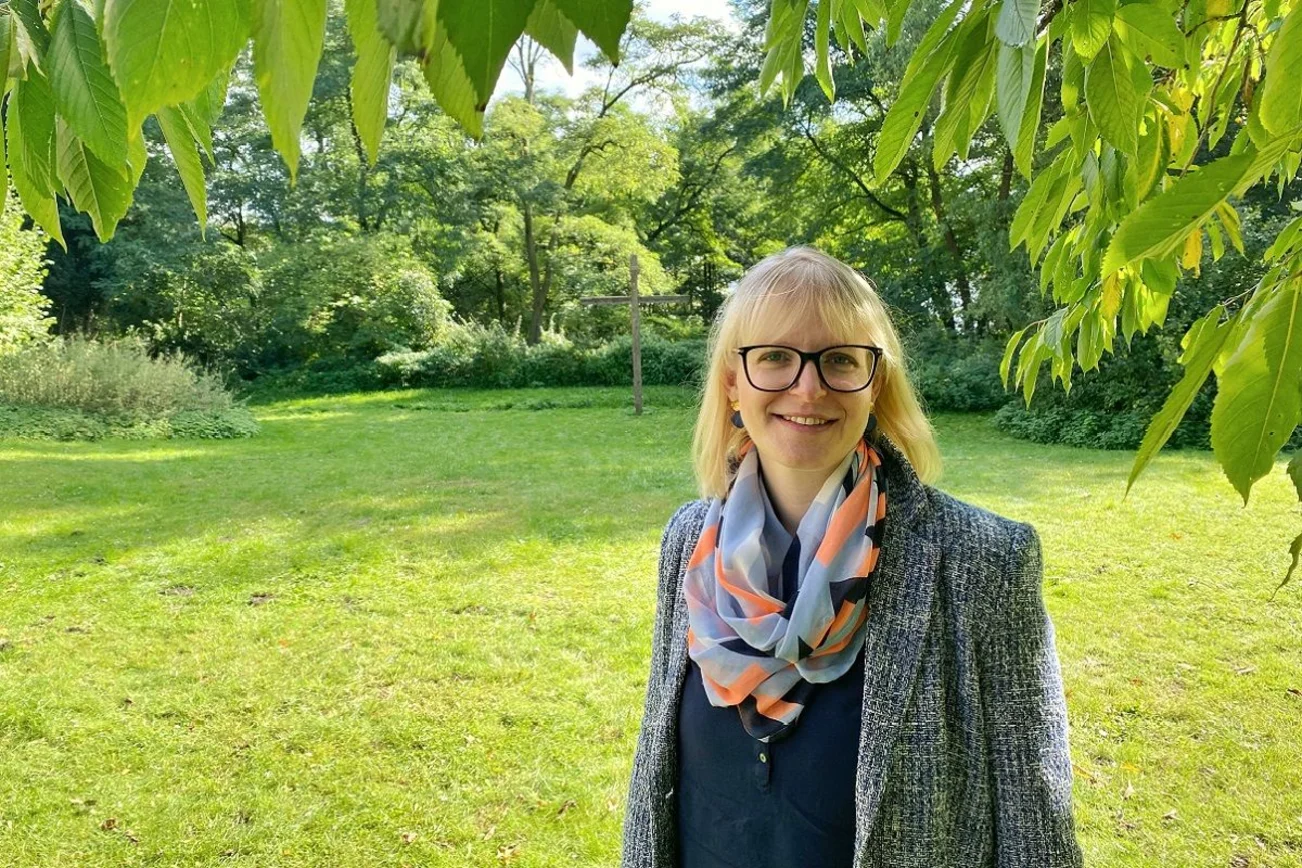 Frau steht lächelt unter einem Baum auf einer Wiese.