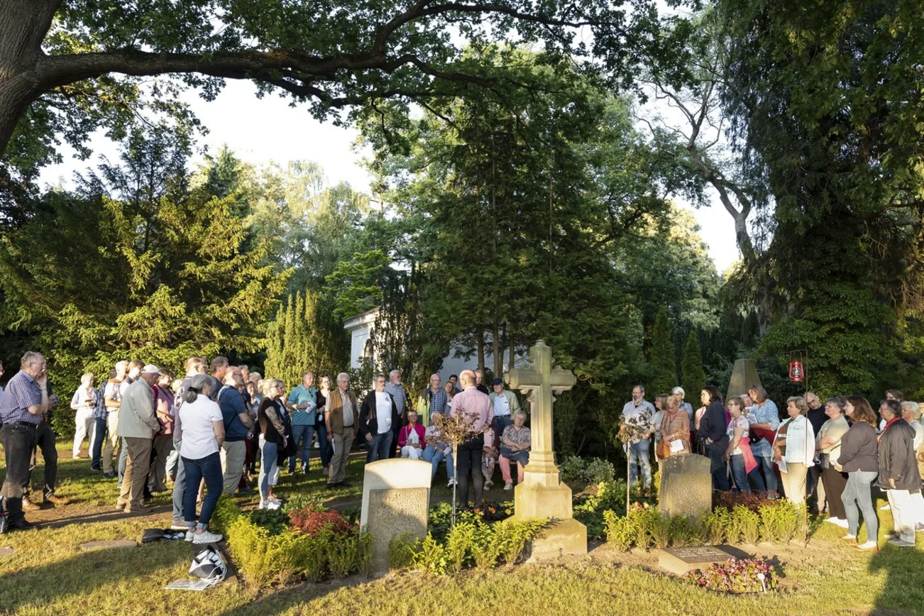 Menschen stehen um ein Grab im Abendlicht