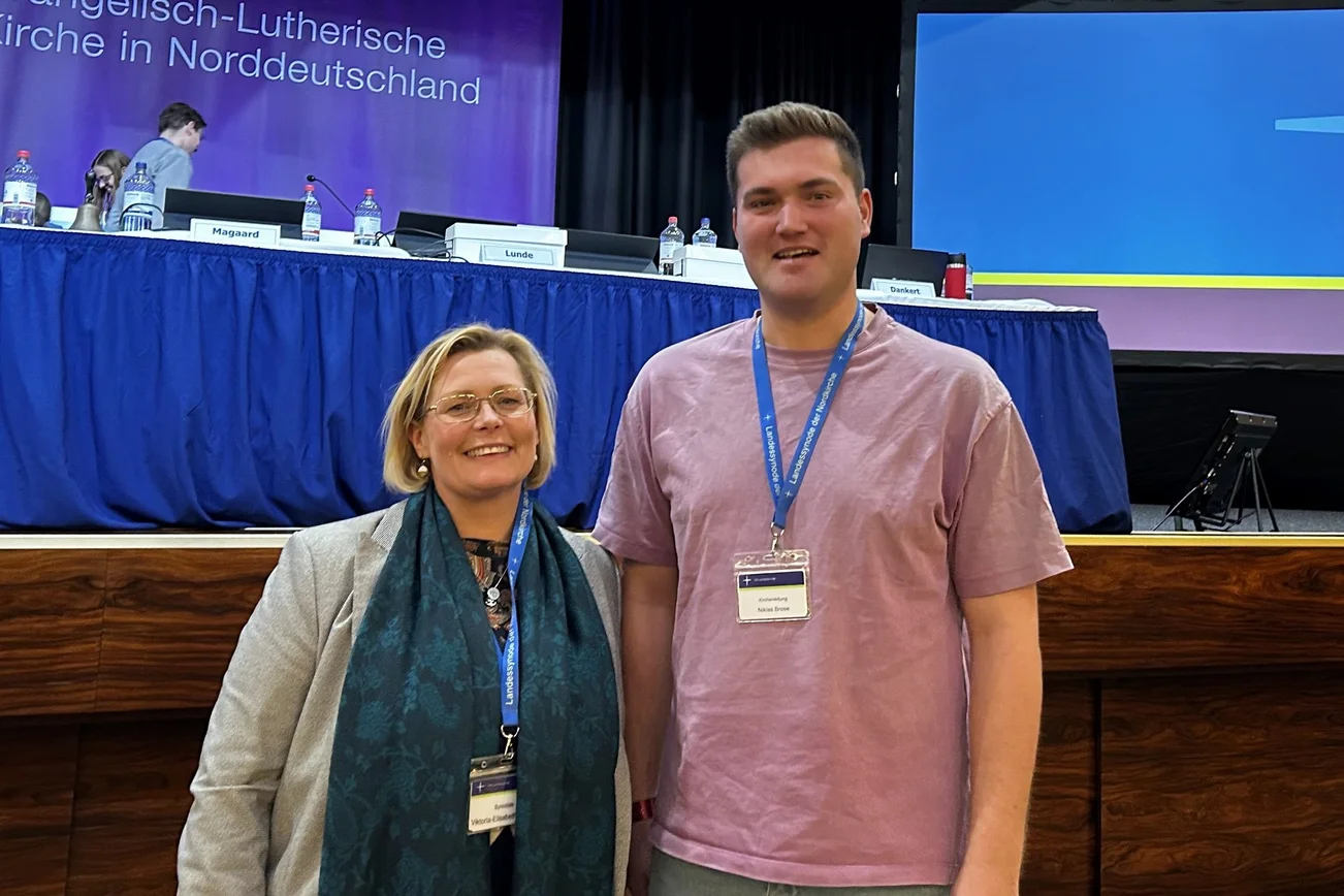 Eine Frau und ein Mann stehen in einem Sitzungssaal.