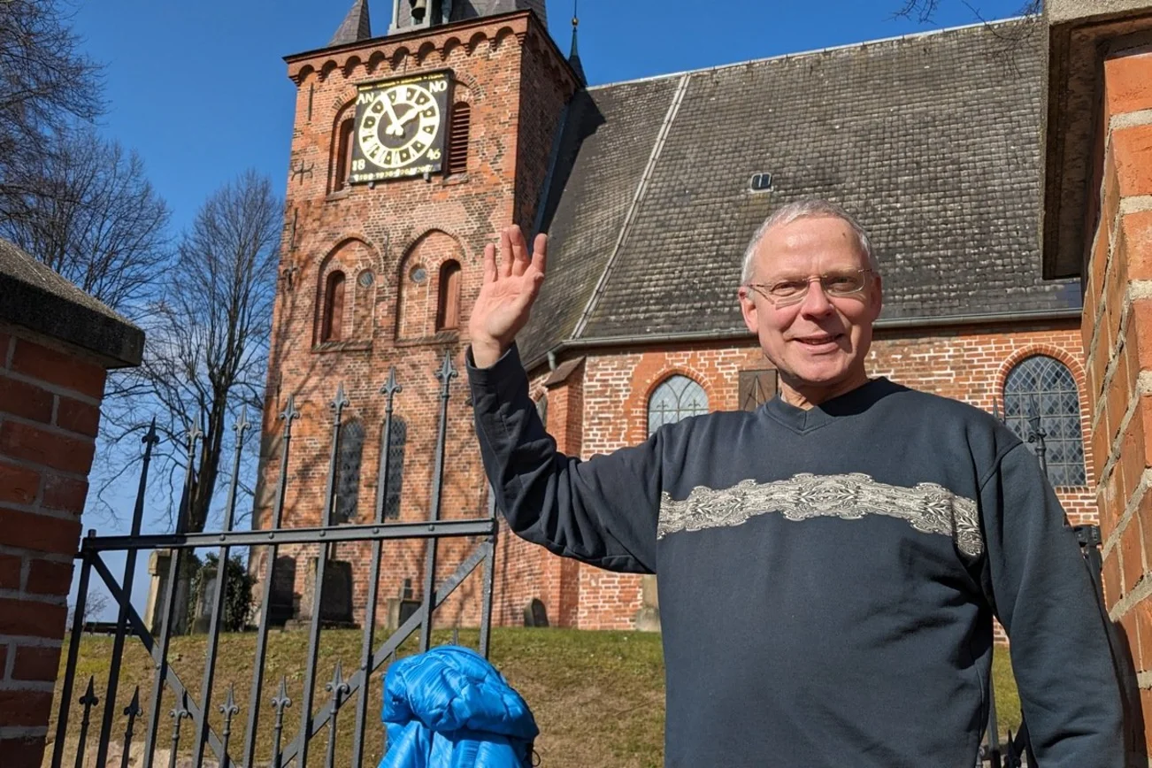 Ein fröhlicher Mann schaut winkend in die Kamera.
