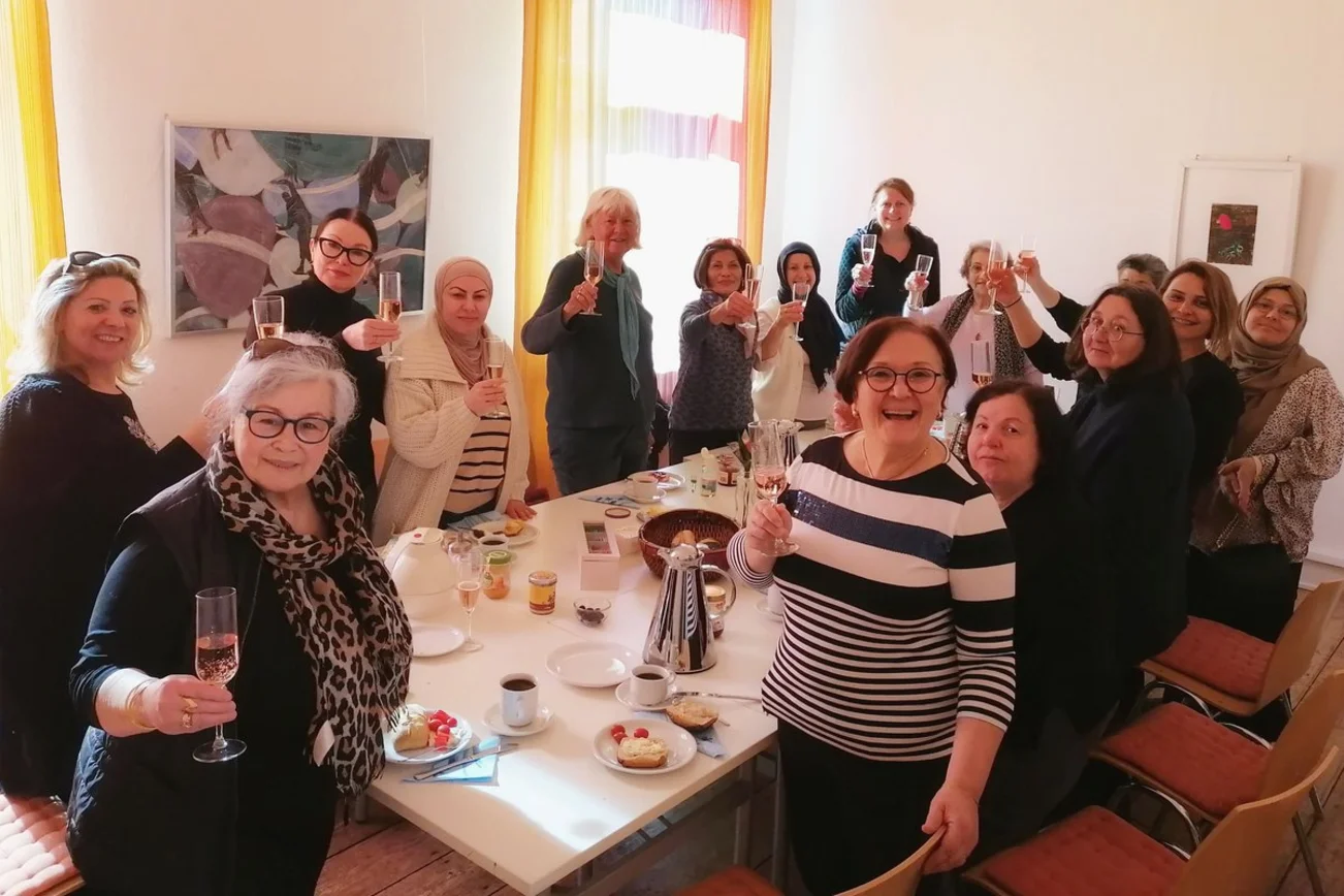 Frauen stehen und sitzen am Tisch und halten Sektgläser in der Hand