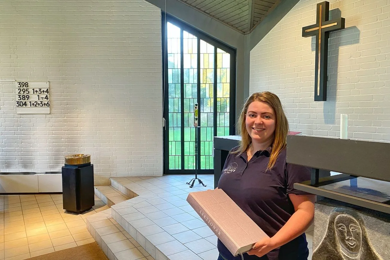 Junge Frau steht in einer Kapelle und hält ein Buch in den Händen. 