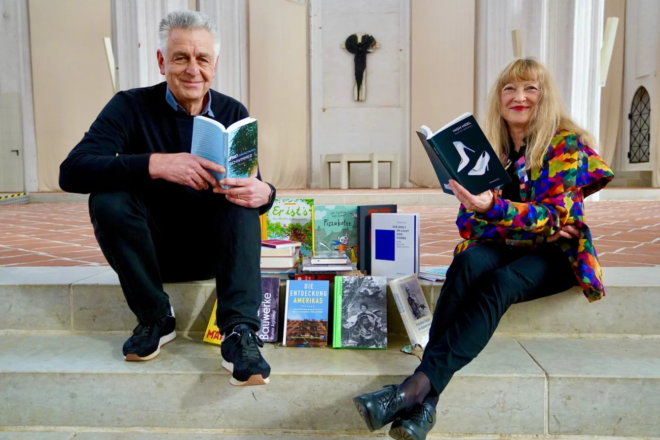 Ein Mann und eine Frau sitzen auf Stufen und haben viele Bücher um sich.