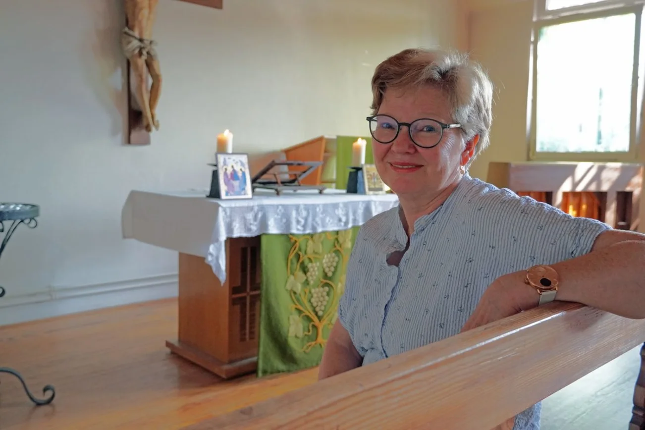 Eine Frau mit Brille und kurzen Haaren sitzt in einer kleinen Kapelle.