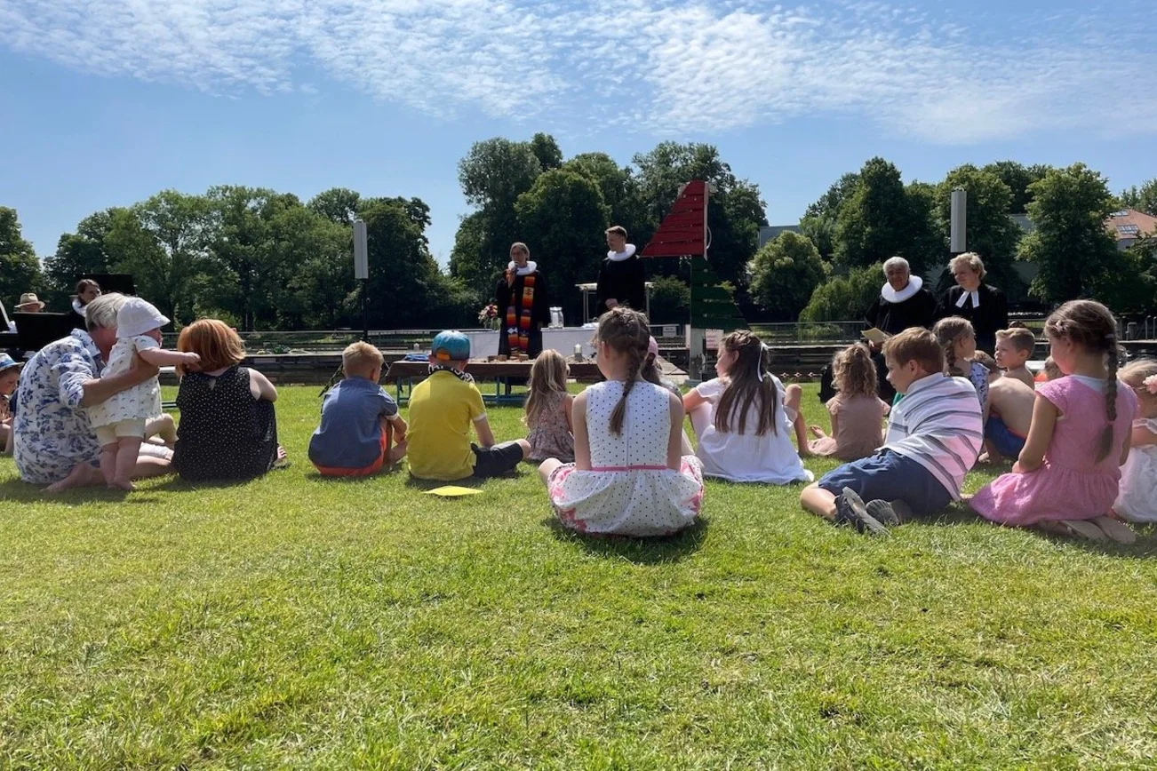 Das Tauffest 2023 im Altstadtbad Krähenteich. Vorne sind Kinder mit ihren Familien sitzend, im Hintergrund Pastorinnen und Pastoren zu sehen. 