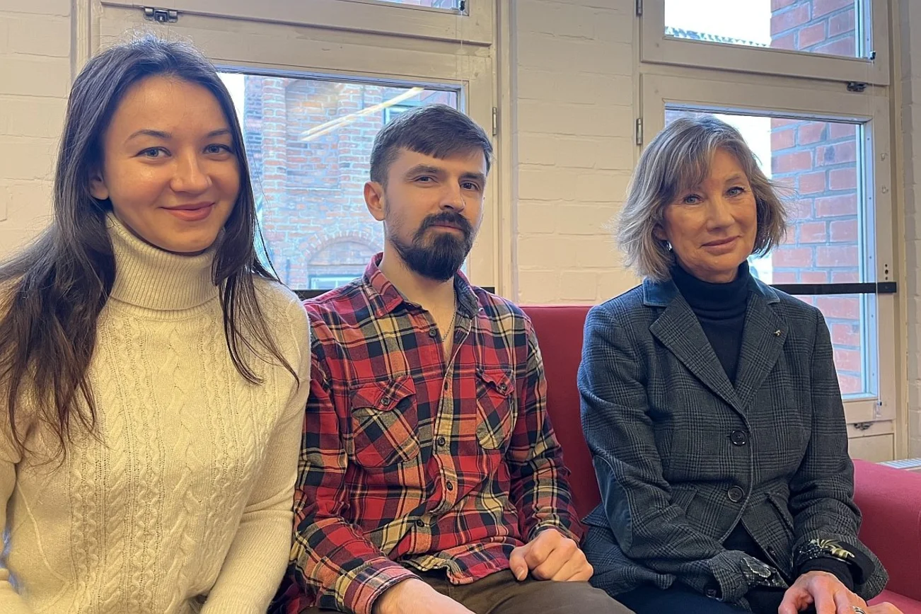 Zwei Frauen und ein Mann sitzen auf einem Sofa und lächeln in die Kamera.