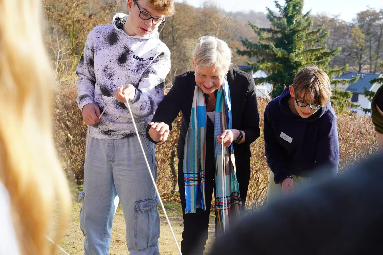 Eine Frau steht mit zwei Jugendlichen konzentriert zusammen und zieht an Seilen.