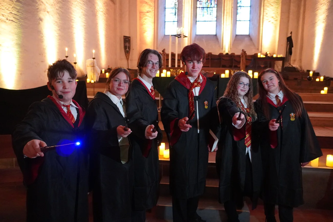 Sechs Jugendliche in Verkleidung halten Zauberstäbe in die Kamera.