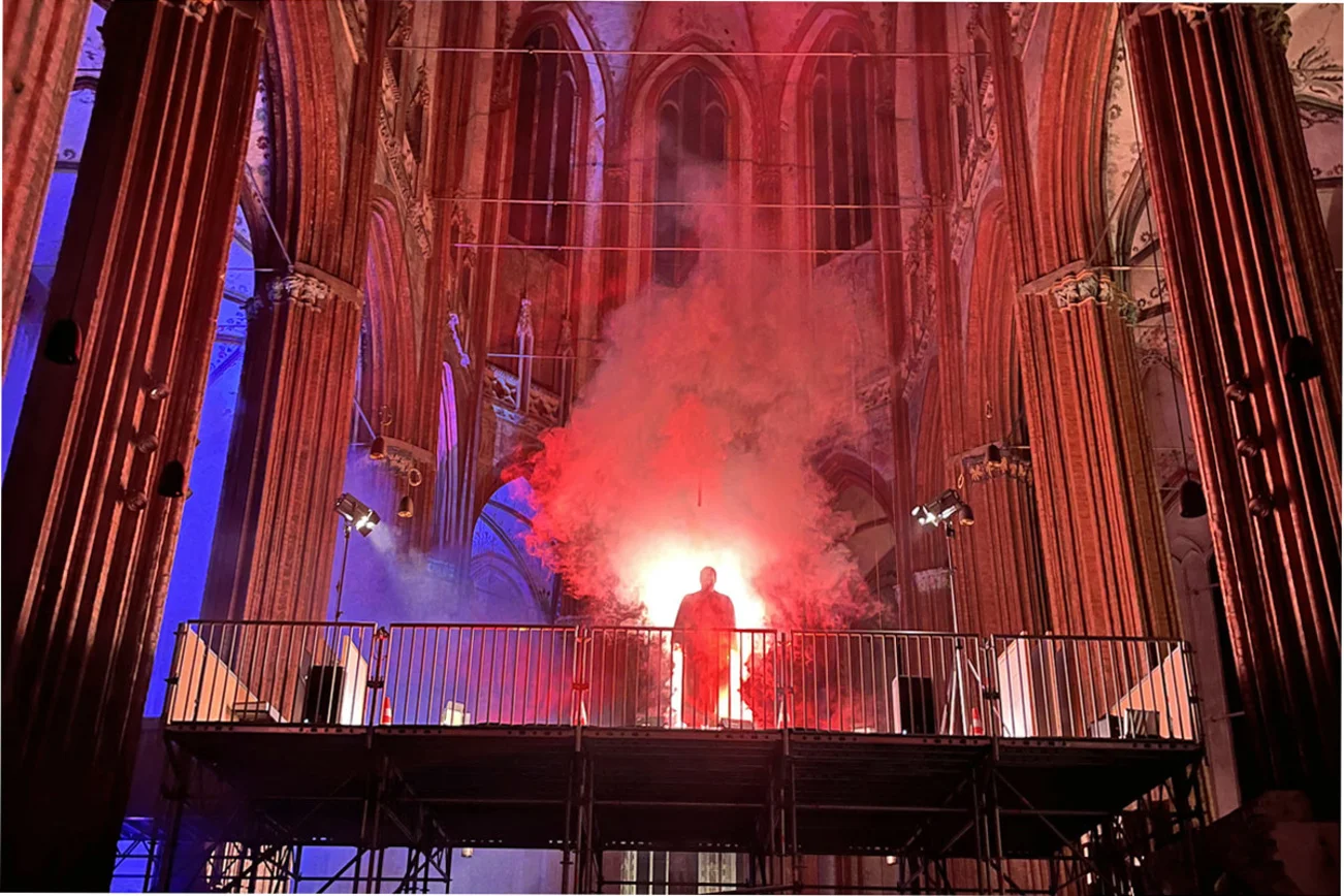 Eine dunkle Gestalt steht auf einem Gerüst im Nebel in einem Kirchenschiff.