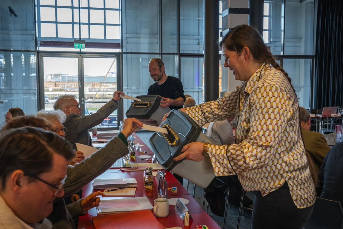 Synodale geben ihre Stimme in eine Wahlbox von zwei Wahlhelfern ein.