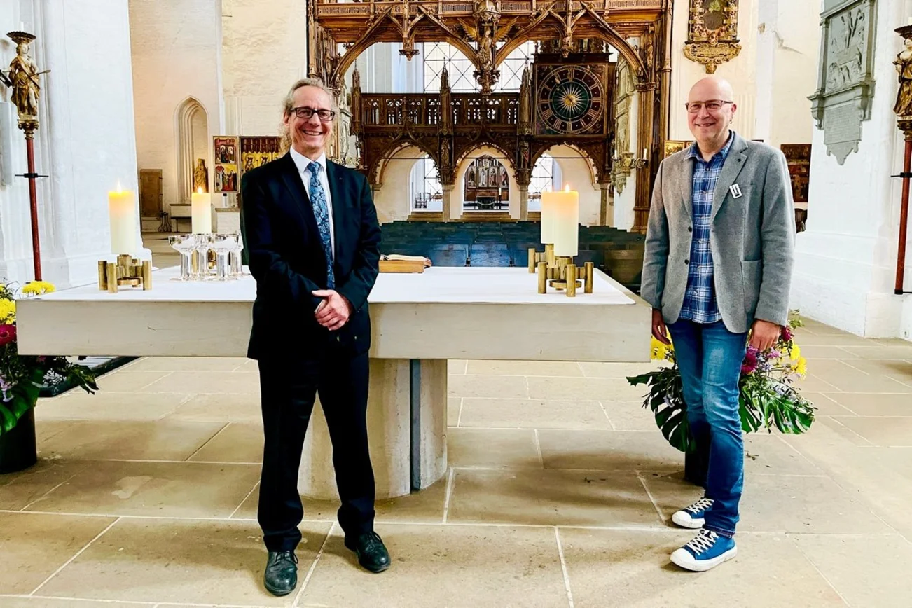 Die beiden Küster stehen im Dom am Altar und lächeln in die Kamera.