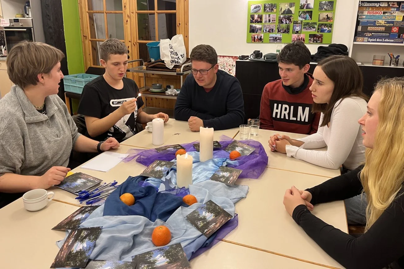 Eine Gruppe junger Menschen sitzt um einen Tisch mit Tüchern und Kerzen. 