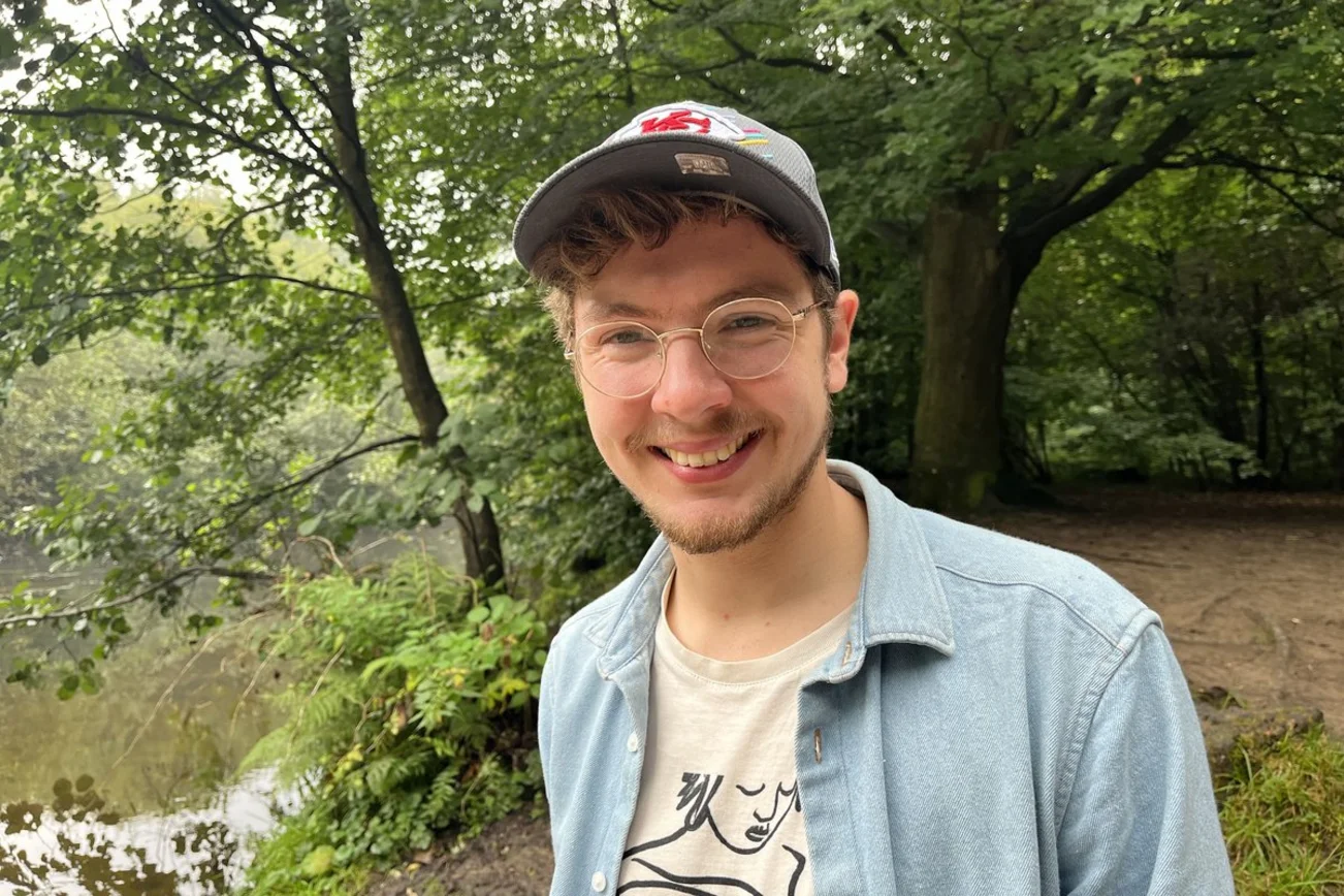 Ein junger Mann mit Brille und Basecap lächelt in die Kamera.