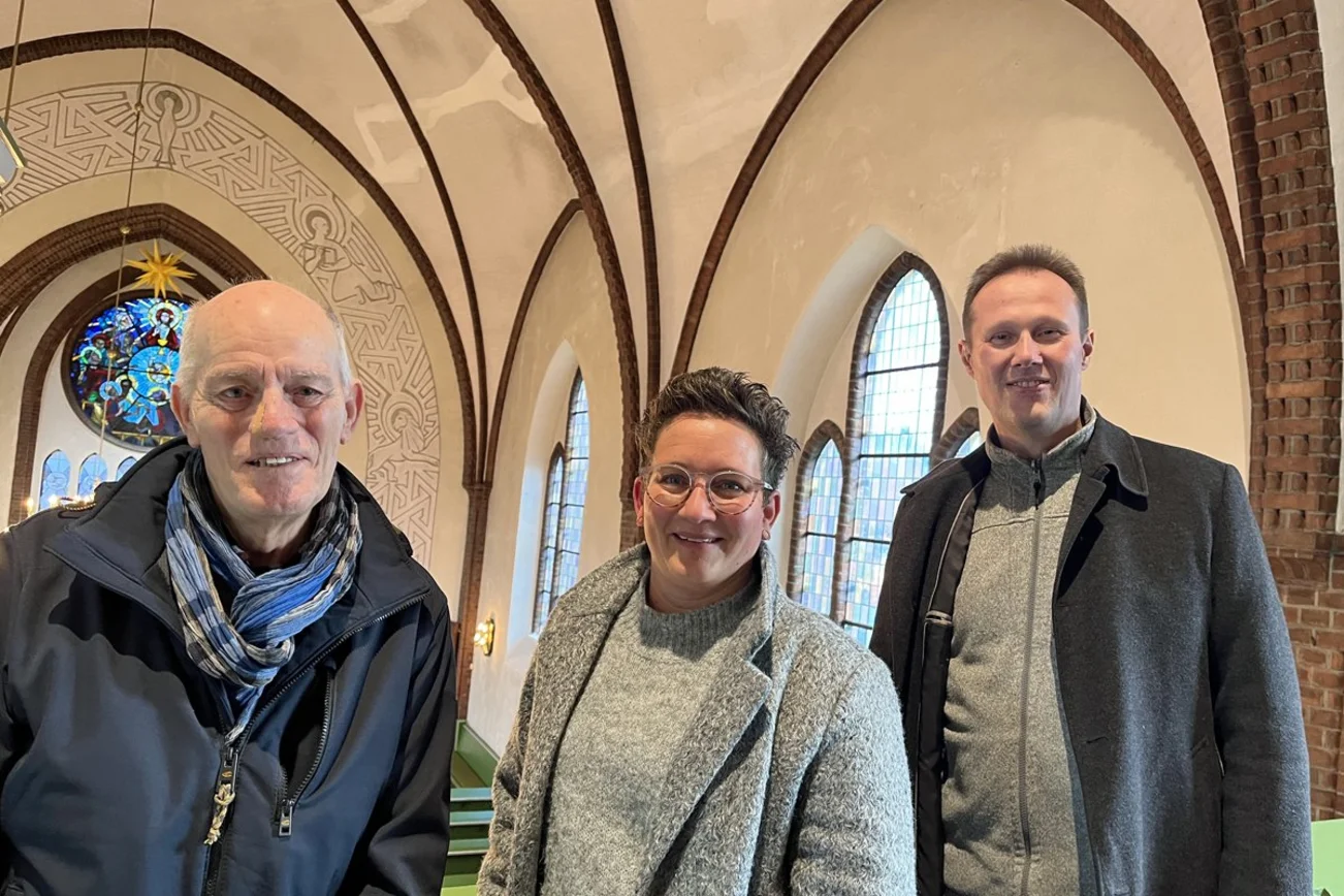 Drei Menschen in der Kirche blicken den Fotografen an.