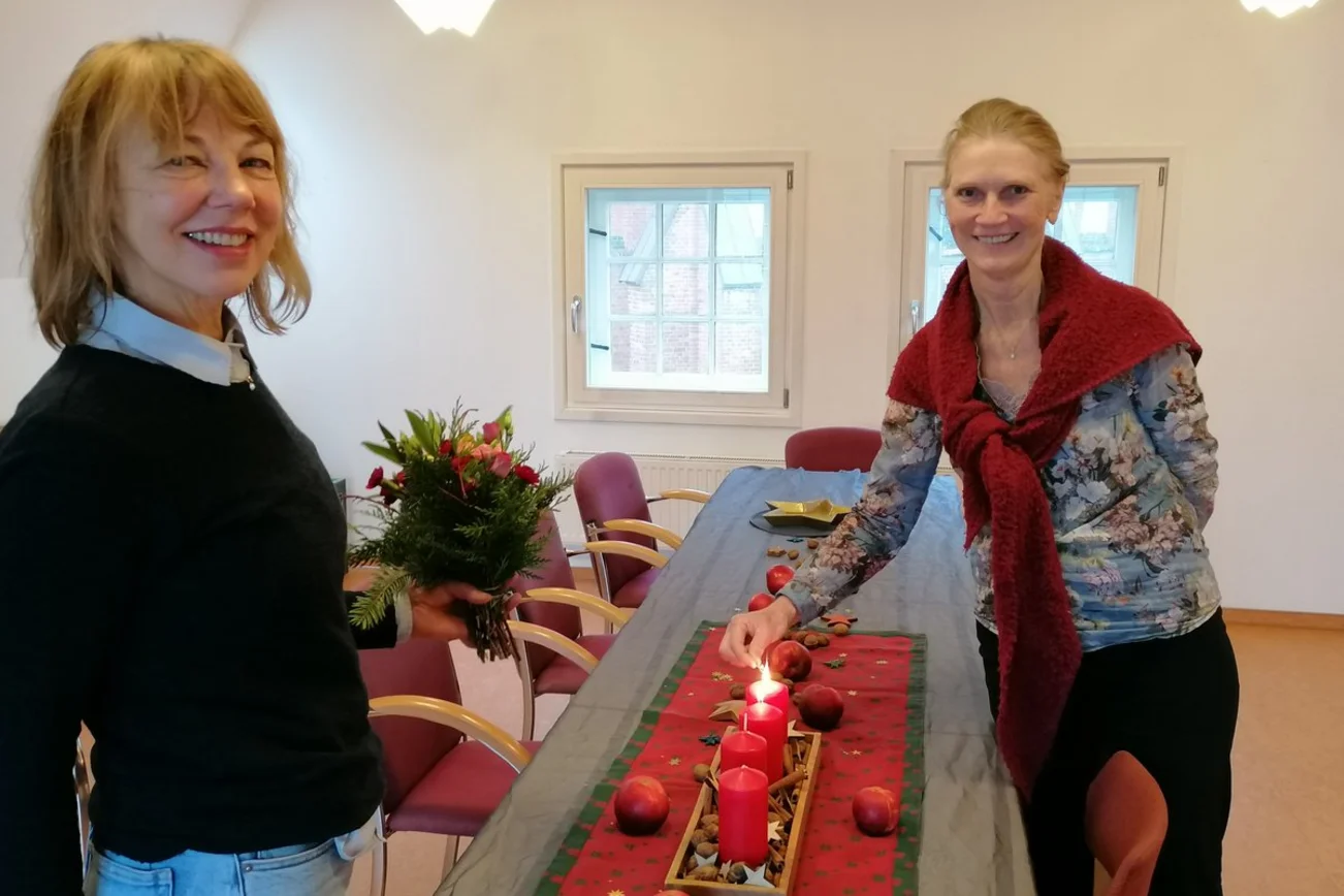 Zwei Frauen lächeln in die Kamera und stehen an einem weihnachtlich geschmückten Tisch.