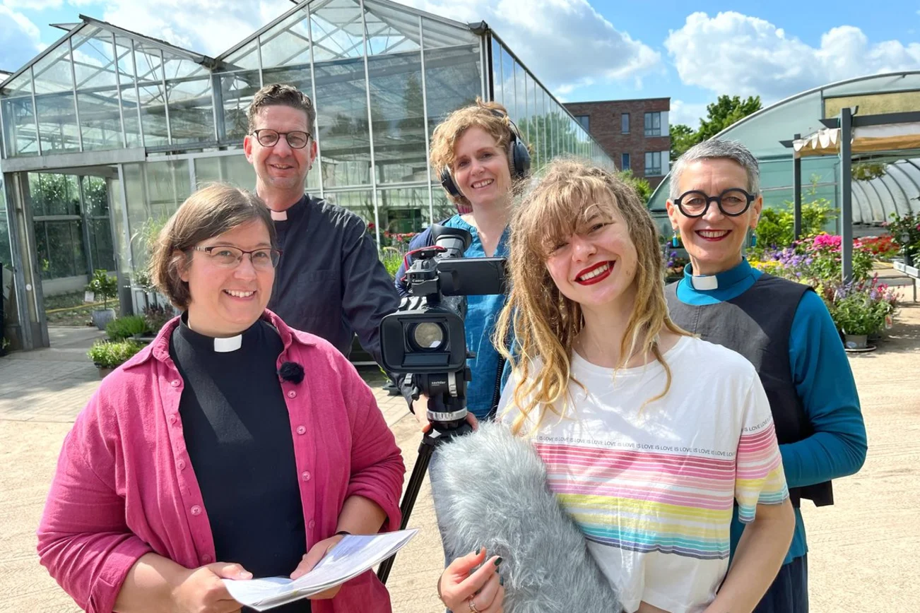 Fröhliche Menschen vom Kirchenkreis Lübeck-Lauenburg mit einer Kamera in einer Gärtnerei. 