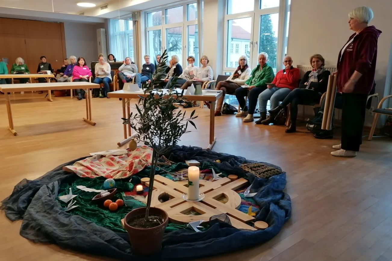 Frauen sitzen am Rand eines Raumes, in der Mitte liegt das WGT-Logo