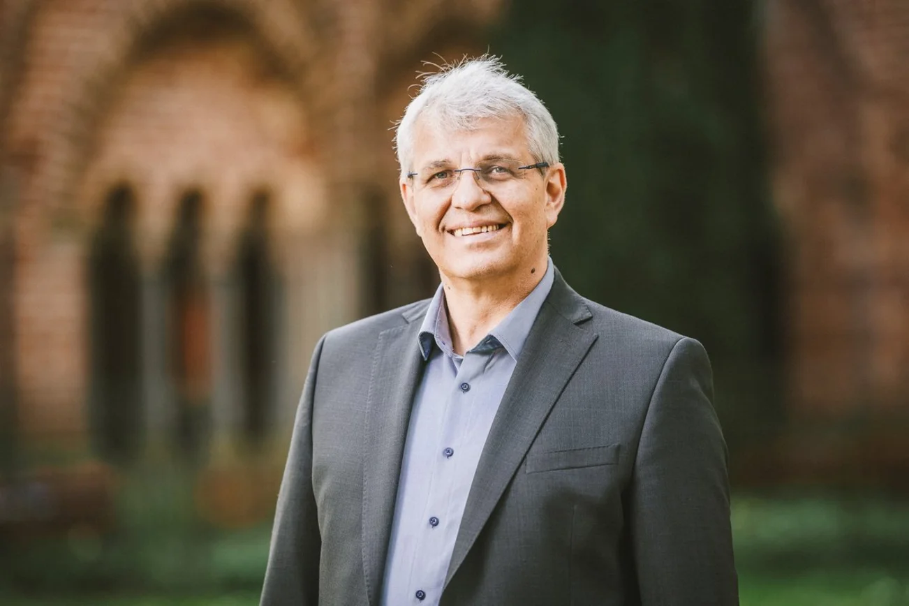 Ein Mann mit grauem Sakko lächelt in die Kamera.