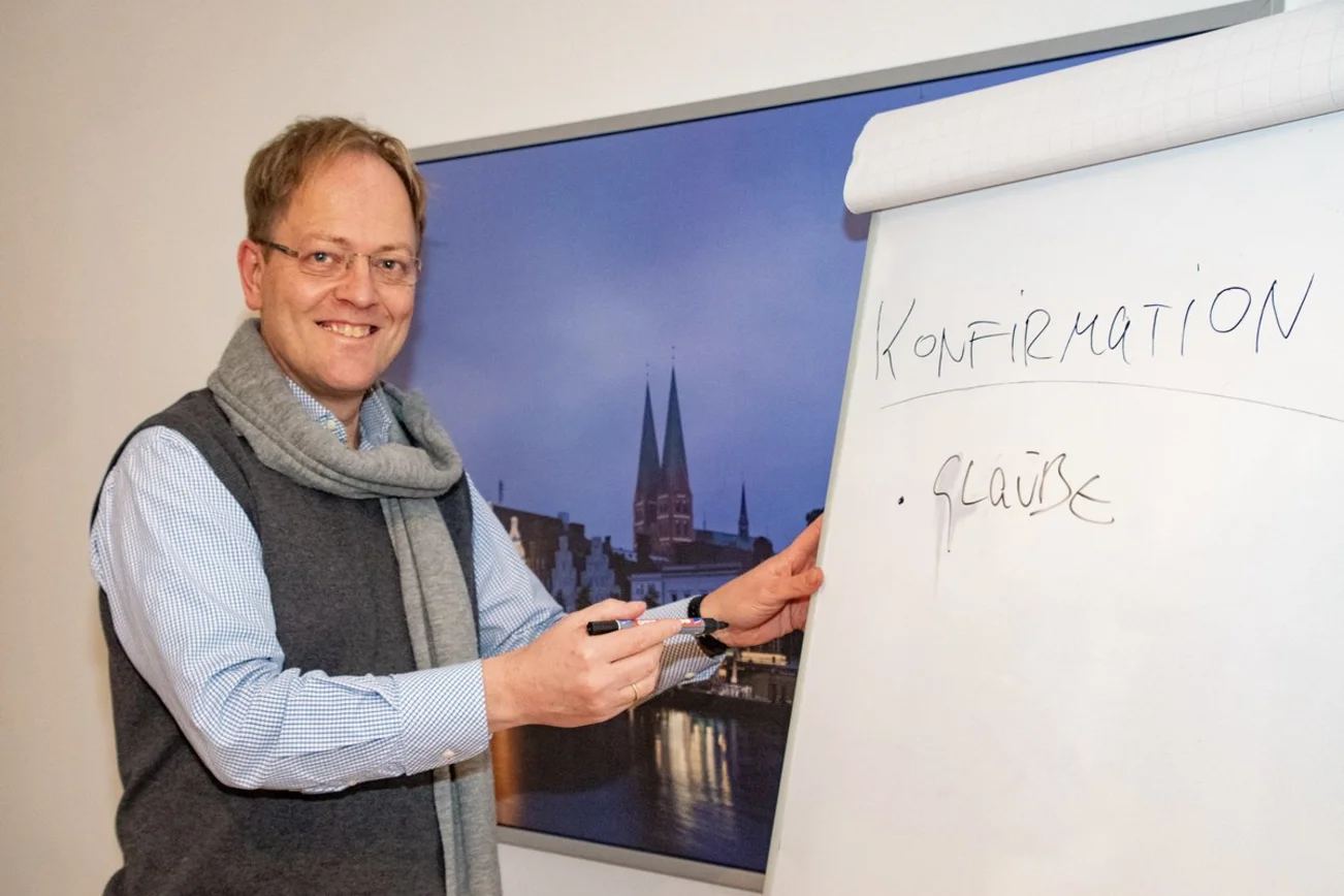 Ein Mann steht lächelnd an einer Tafel.
