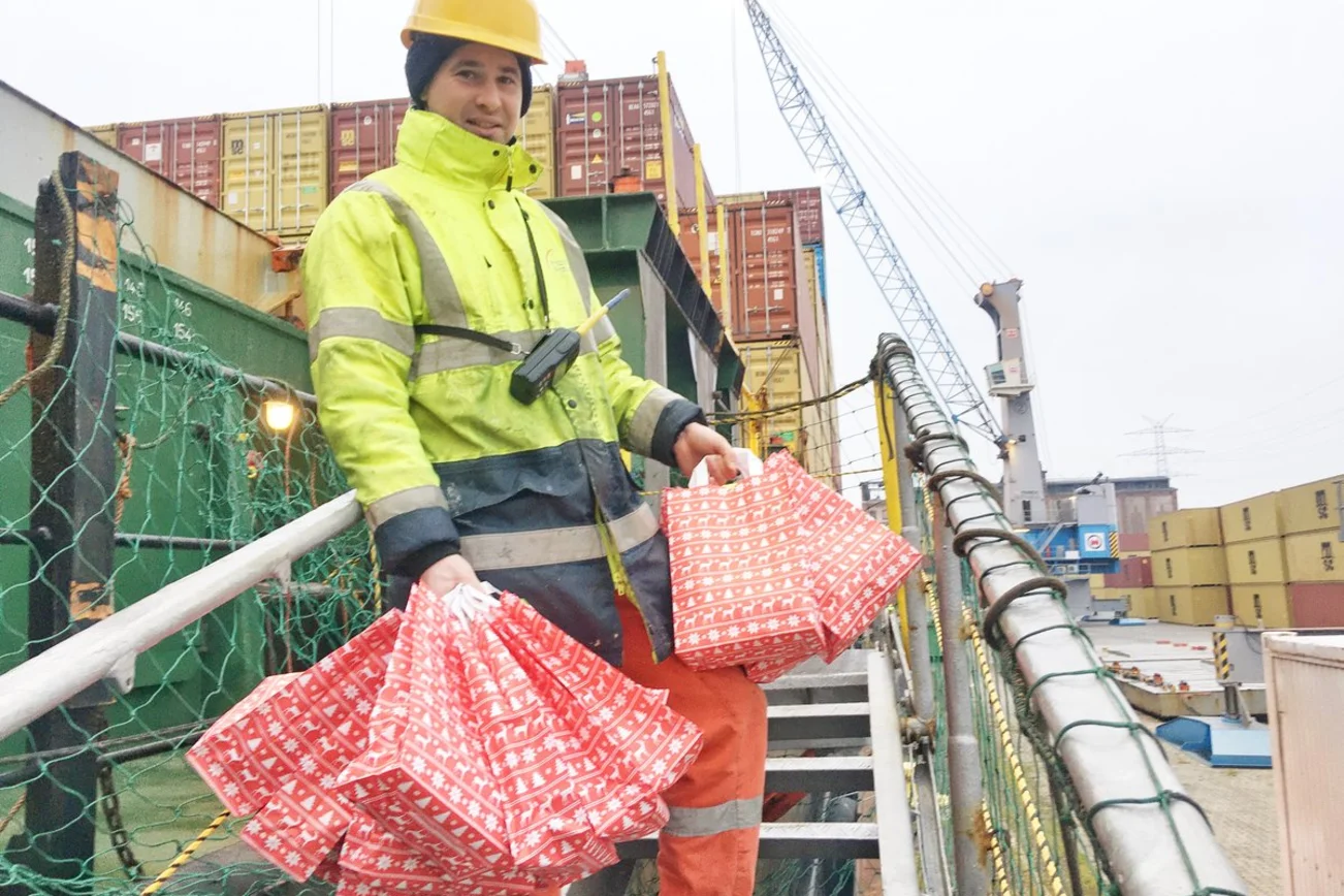 Ein Mensch steht mit Tüten an einem Schiff