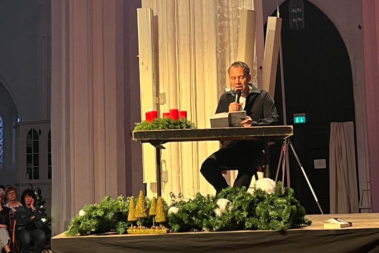 Ein Mann sitzt an einem Tisch und liest mit Mikro aus seinem Buch.