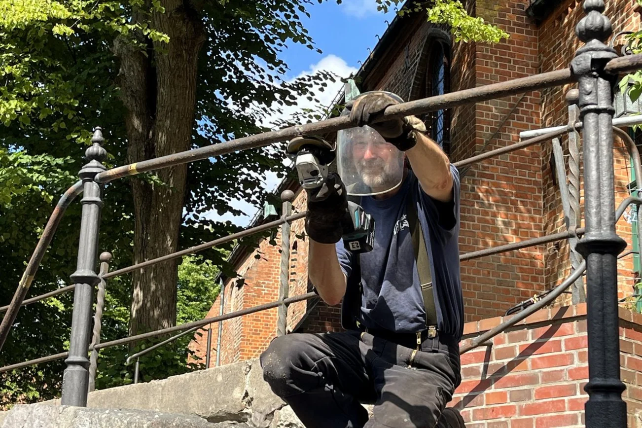 Ein Arbeiter schleift einen Metallhandlauf vor einer Kirche