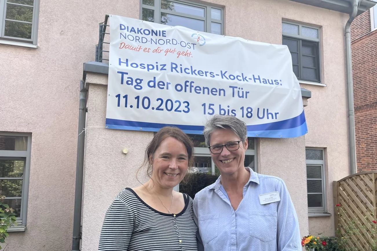 Zwei Frauen stehen vor einem Gebäude mit einem Schriftbanner