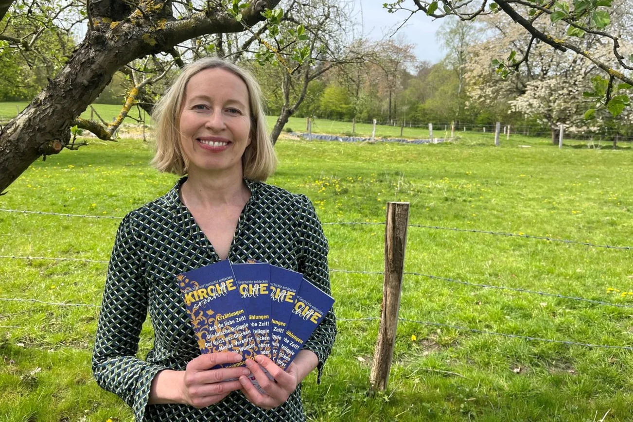 Eine Frau steht vor einer Wiese und hält einige Flyer in der Hand