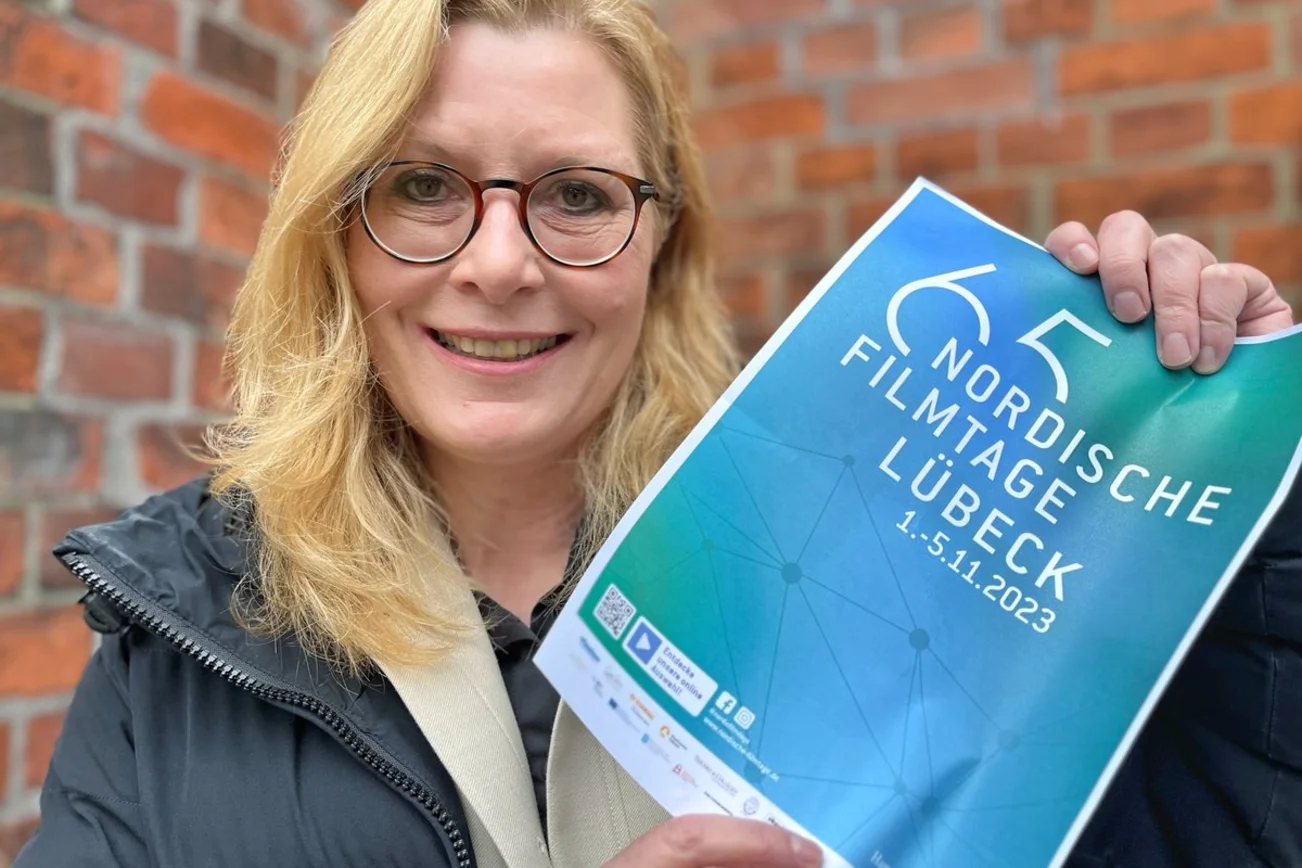 Eine Frau hält ein Plakat der Nordischen Filmtage in den Händen und blickt freundlich in die Kamera. 