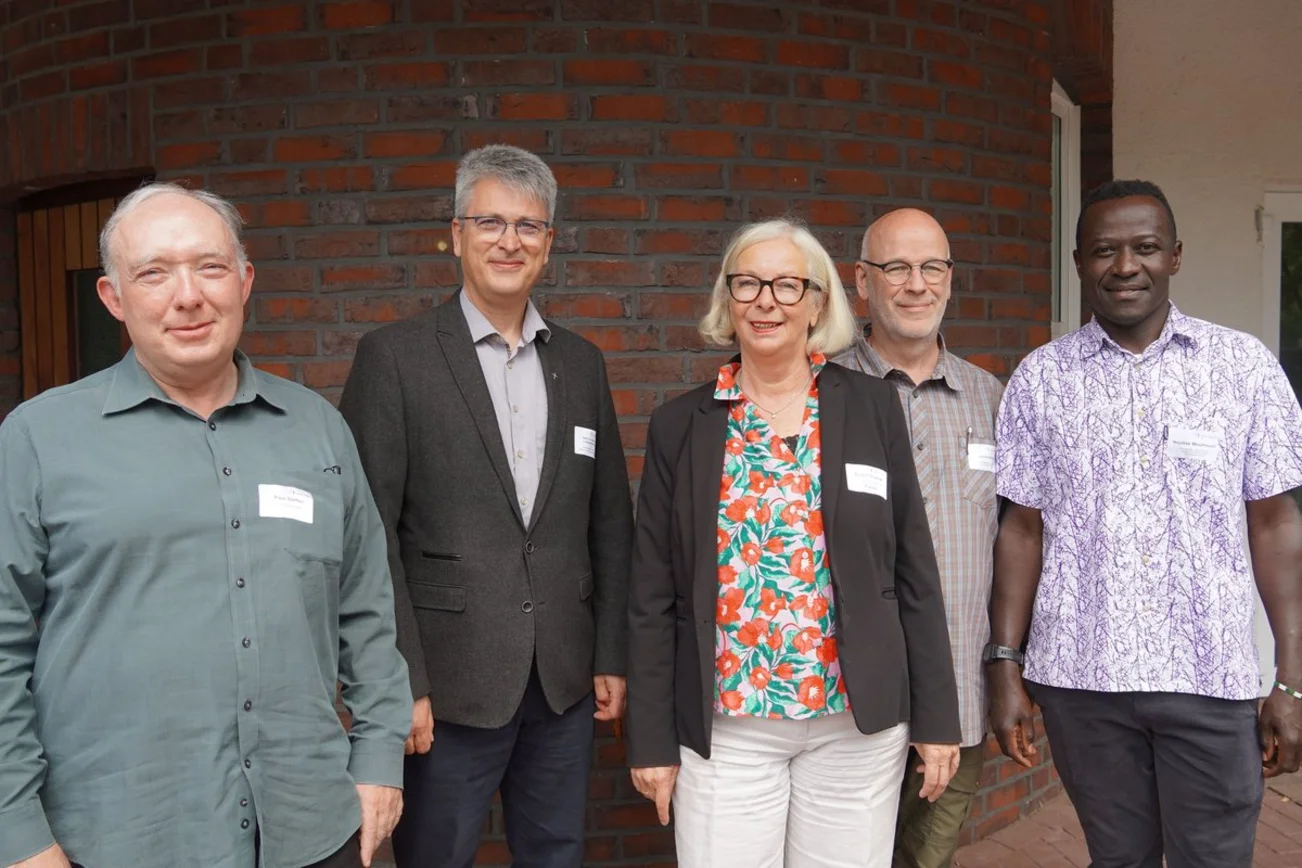Vier Männer und eine Frau stehen vor eine Backsteinwand.