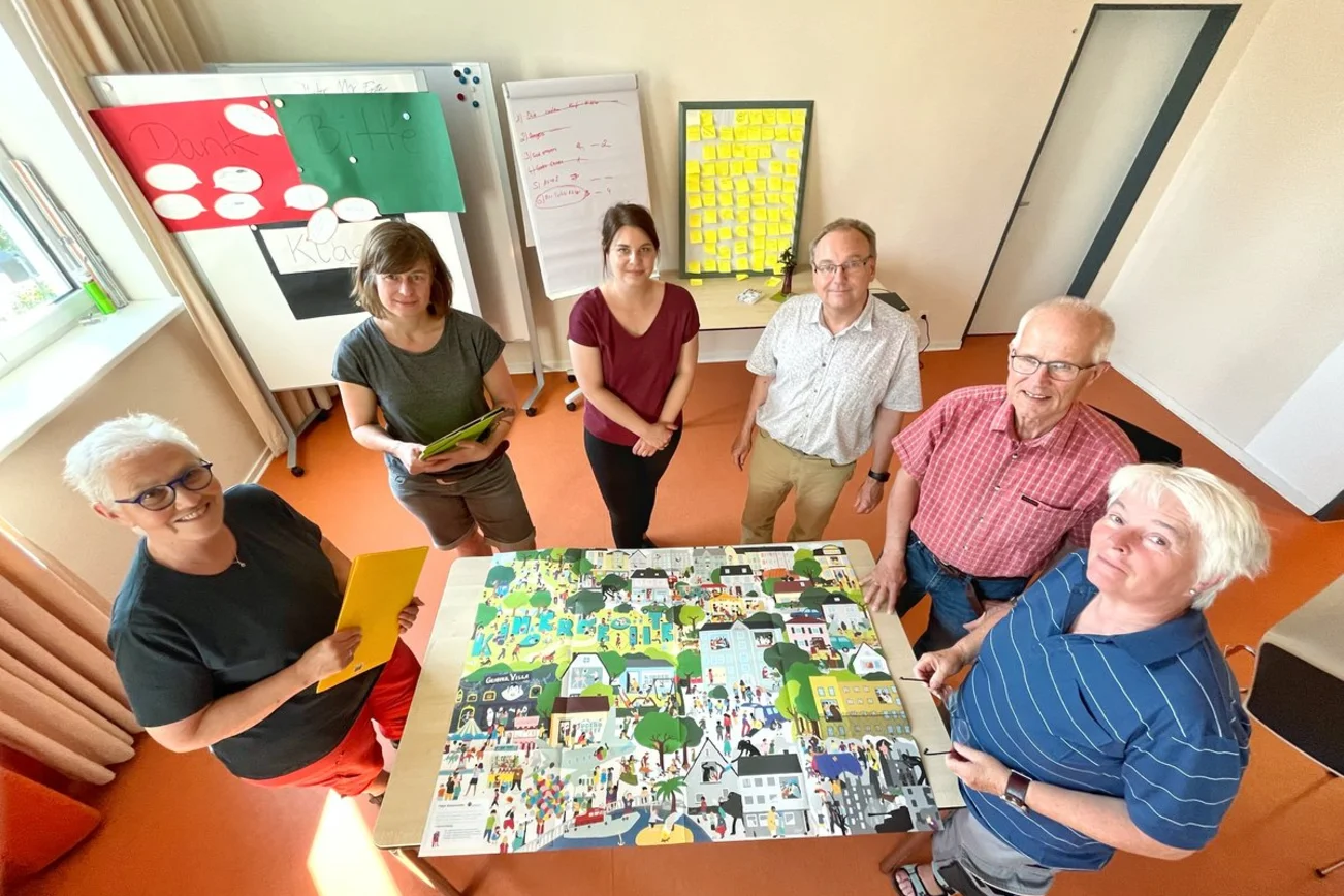 Menschen befinden sich in einem Raum und blicken in die Kamera. 