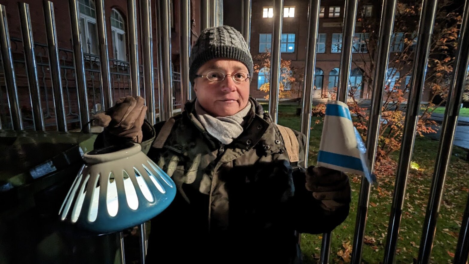 Eine Frau steht vor einem Zaun mit einem Licht in der Hand. 