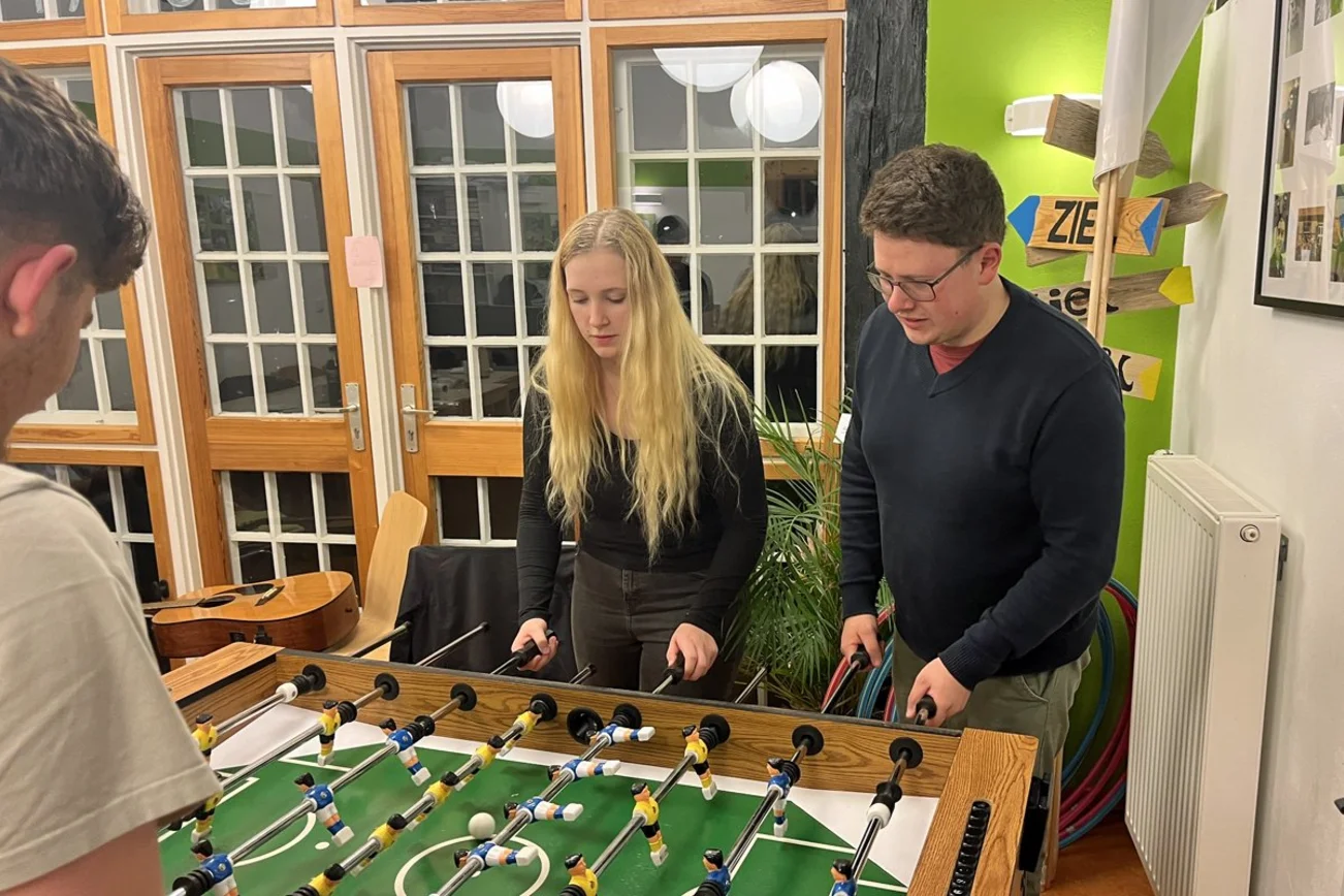 Drei junge Menschen spielen Tischkicker. 