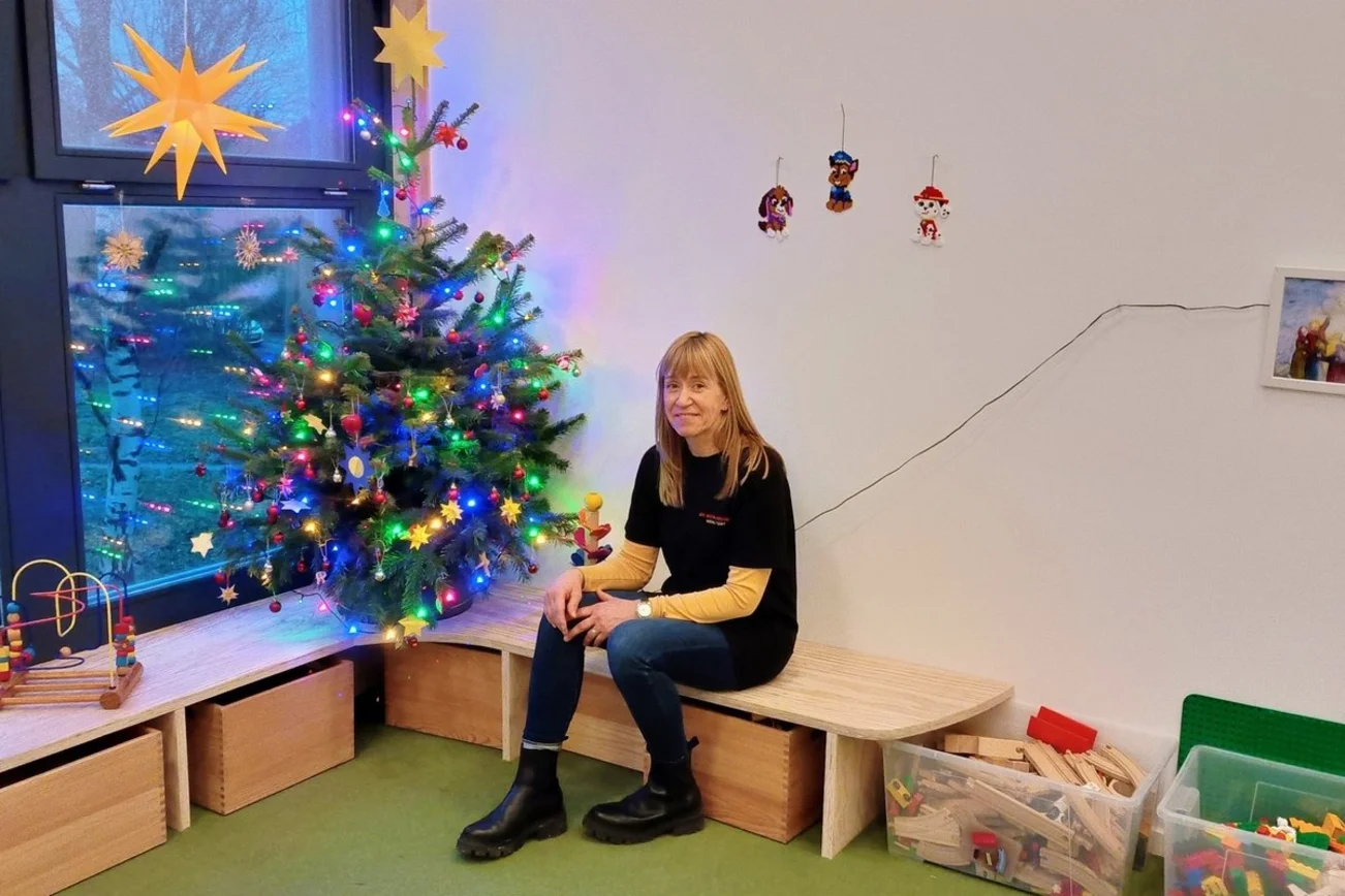 Eine Frau sitzt auf einer Holzbank vor einem geschmückten Weihnachtsbaum.
