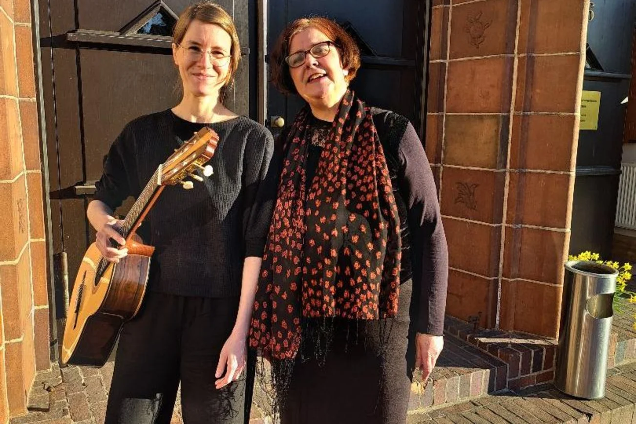 Zwei Frauen stehen vor einem großen Tor und eine Frau trägt eine Gitarre